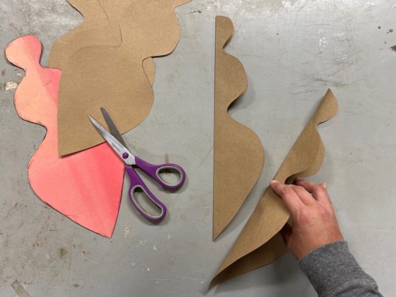 The hand of a person folding a brown cut out shape in half.